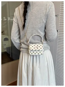 Vue de dos d’un modèle portant un petit sac blanc à pois noirs, avec papillon rose et chaîne dorée