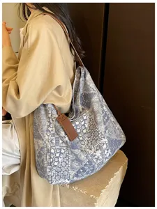 Una donna indossa una borsa a spalla blu e bianca fantasia, con tracolla e targhetta in pelle marrone