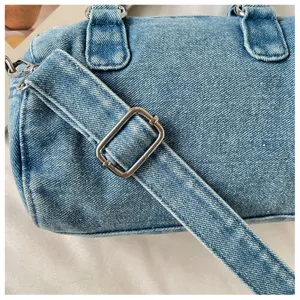 Gros plan sur la texture du denim délavé, la bandoulière réglable et la boucle argentée du sac