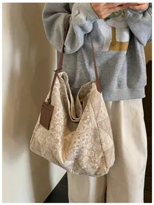 Borsa crema in tessuto a motivi marroni, tracolla lunga in pelle e porta carte, indossata a spalla