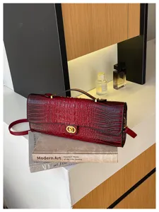 Bordeauxrode tas met krokodillenstructuur en gouden sluiting, gestyled op boeken naast parfumflesjes