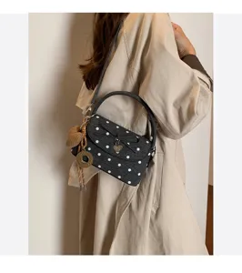 Borsa scura a pois bianchi indossata sopra un cappotto beige, con ciondoli decorativi in vista