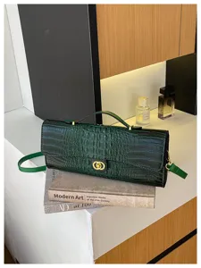 Detail van een groene tas met krokodillenreliëf, gouden dubbele ringsluiting en korte handgreep