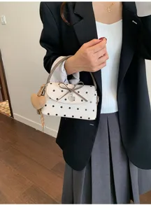 Modella con borsa bianca a pois neri, manici marroni, fiocco e pendenti decorativi a cuore
