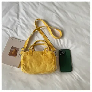 Vue de dessus d’un sac en toile jaune avec poignées et bandoulière sur un linge de lit blanc