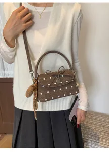 Dettaglio della borsa marrone a pois bianchi, con fiocco, ciondolo a cuore e nappa intrecciata