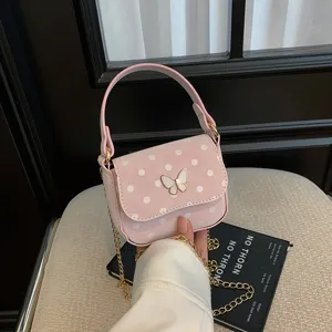Small pink polka-dot handbag with butterfly clasp and gold chain strap, shown being held