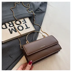 Close-up van een bruine kunstleren tas met klep, gouden ketting en metalen handgreep