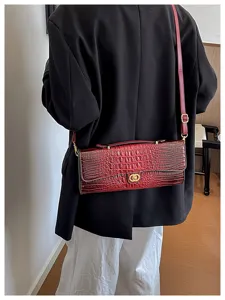 Rode tas met krokodillenstructuur over zwarte blazer, met goudkleurige sluiting met dubbele ring