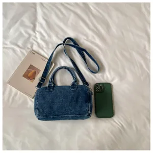 Sac bleu délavé posé à plat sur un linge blanc, avec bandoulière réglable et boucles métalliques
