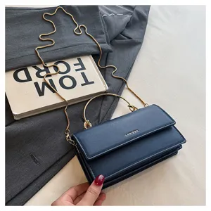Detail van een marineblauwe tas met klep, gouden ketting en ringvormig handvat, op stof gelegd