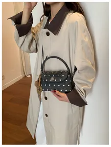 Borsa grigio scuro a pois bianchi, con fiocco e ciondolo a cuore, abbinata a un trench chiaro