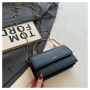 Detail van een zwarte tas met klep en gouden ketting, liggend op stof naast een boek