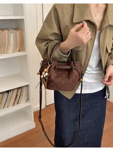 Sac brun à pois en suédine, avec bandoulières en cuir, détails dorés et pompon de perles en bois