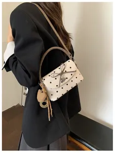 Borsa a pois color crema indossata a spalla, con fiocco, chiusura a cuore e ciondolo intrecciato