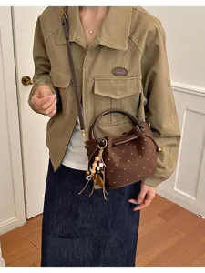 Sac brun effet daim à pois clairs, porté en bandoulière avec pompon de perles et détails dorés