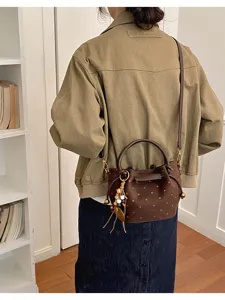 Vue de dos d’un modèle portant un sac brun à pois, avec anse, bandoulière et breloques en bois