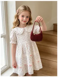 Burgundy mini handbag with long fringe, held by a child beside a white floral lace dress