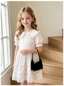 A girl models a floral lace-trimmed dress beside wooden steps, carrying a black fringed handbag