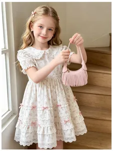 A child holds a blush pink fringed handbag beside a white floral dress on a wooden staircase