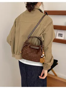 Vue de dos d’un modèle portant un sac brun effet daim à pois, avec breloque en bois et perles