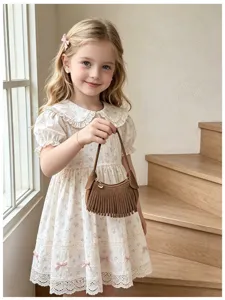 Child model holding a brown suede-look mini bag with long fringe and gold-tone hardware indoors