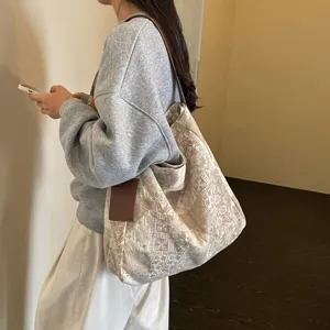Ampia borsa tote beige in tessuto jacquard, con manici in pelle marrone, portata a spalla