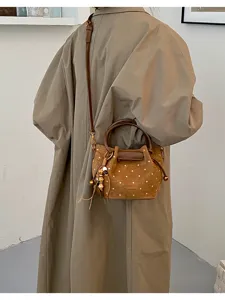 Vue de dos d’une personne portant un sac brun à pois, avec pompon et détails métalliques dorés