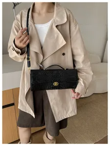 Zwarte tas met krokodillenstructuur en goudkleurige details, gedragen bij een beige trenchcoat