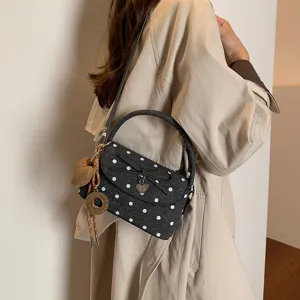 Borsa nera da donna a pois bianchi, con fiocco e ciondoli, indossata da una modella
