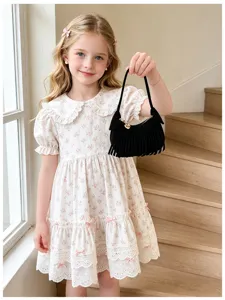 A girl holds a black fringed handbag beside a tiered floral dress in a bright stairwell.