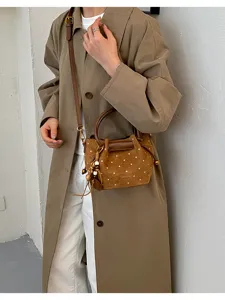 Sac seau brun à pois blancs, porté avec un trench, avec sangles en cuir, détails dorés et breloque