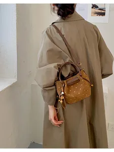 Femme portant un sac bandoulière brun à pois crème, avec pompons et détails métalliques dorés
