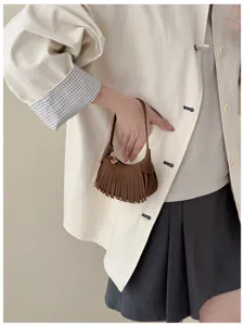Close-up of a brown suede-texture mini bag with fringe and a small metal heart charm, held by hand
