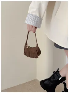 Lifestyle view of a hand holding a brown suede-look fringed bag with a gold heart charm