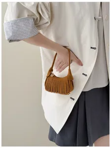 Close-up of a brown suede-look bag with fringe, a gold charm and short handle, held by hand