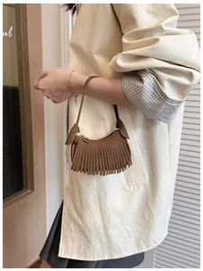 Close-up of a brown suede-textured bag with fringe and a slim strap carried beside a cream coat
