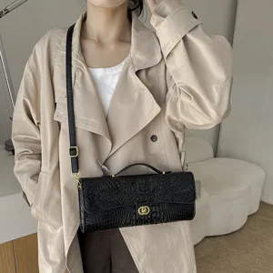 Zwarte crossbodytas van PU met krokodillenprint en gouden sluiting, gedragen over een lichte jas