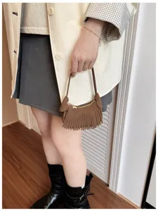 Lifestyle view of a brown suede-look bag with fringe, gold zipper and clasp, carried by hand
