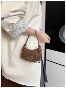Close-up of a brown suede-look crescent bag with dense fringe, shown carried by hand