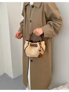 Une personne porte un sac seau crème à pois bruns, avec des anses en cuir et un pompon suspendu.