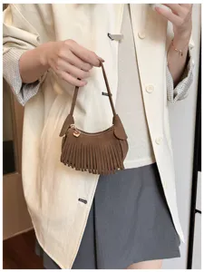 Brown fringed mini bag with a short handle and heart charm, shown carried against light clothing
