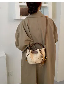 Vue de dos d’un modèle portant un sac crème à pois bruns, bordure brune, détail bambou et pompon.