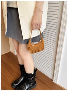 Brown crescent bag with suede-like texture and fringe, held by its short handle with gold hardware