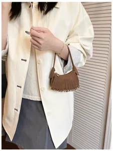 A model holds a small brown suede-look crescent bag with fringe trim and a top zipper