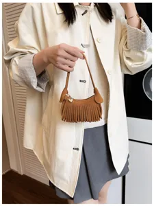 Model holding a brown suede-look mini shoulder bag with fringe trim, zipper, and heart charm