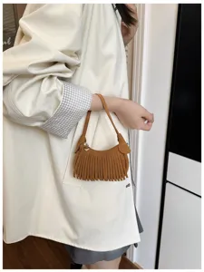Lifestyle view of a model carrying a brown suede-look crescent bag with long fringe and a slim strap