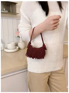 Model holding a burgundy suede-look mini bag with fringe against a softly lit kitchen backdrop