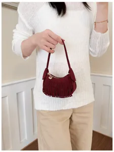 Woman holding a burgundy suede-look fringe bag with a gold zipper and heart charm