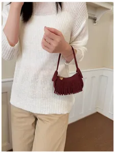 Model holding a small burgundy suede-look shoulder bag with fringe and a gold heart zipper pull